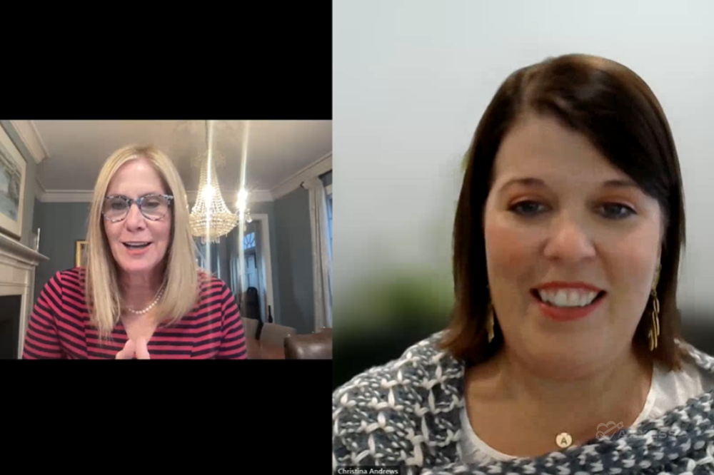 A split screen displays two women engaged in a video call. On the left, a blonde woman with glasses, dressed in a red and black striped shirt, is actively speaking. On the right, a brunette woman, adorned with a gray knitted scarf and gold earrings, is also contributing to the conversation.