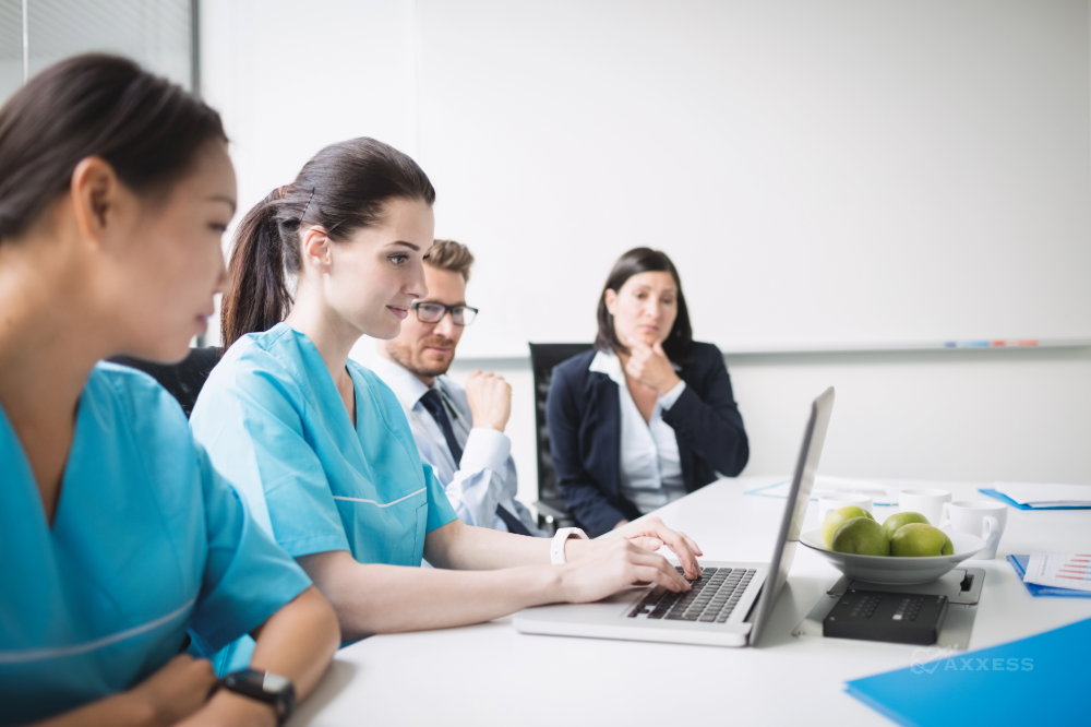 Healthcare professionals and office staff sit around a conference table as one team member works on a laptop during a collaborative care planning meeting.